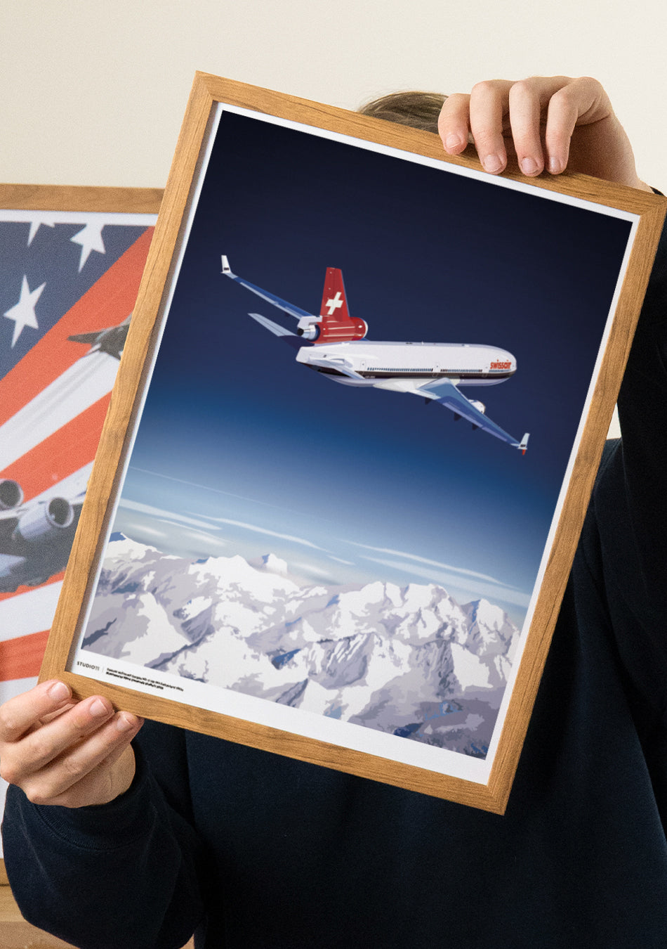 Njord holding the premium Studio11 Swissair MD-11 poster, featuring the aircraft flying over the Swiss Alps in a retro-inspired illustration.