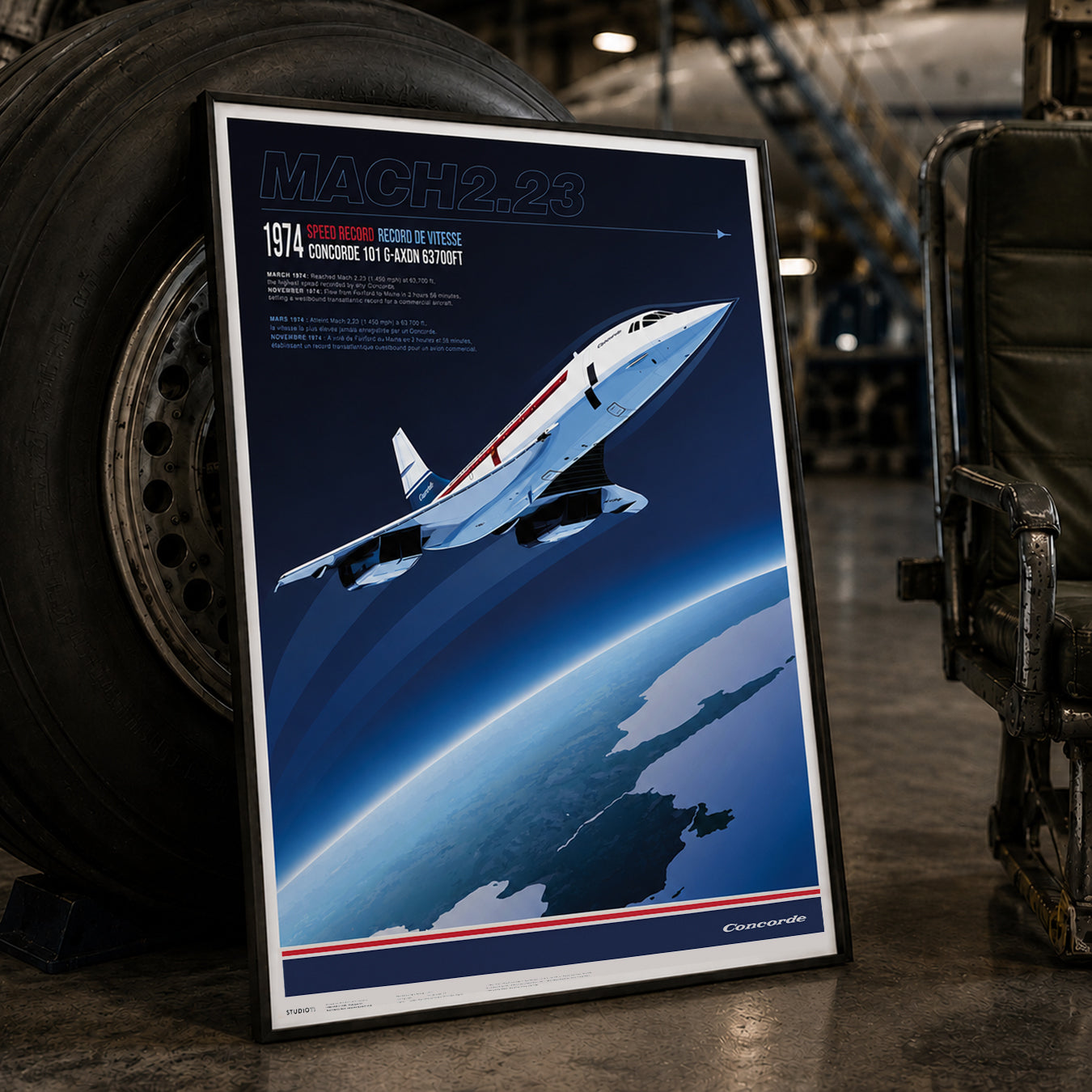 Framed Concorde Prototype 101 aviation poster displayed inside an industrial aircraft hangar beside a Concorde landing gear wheel.